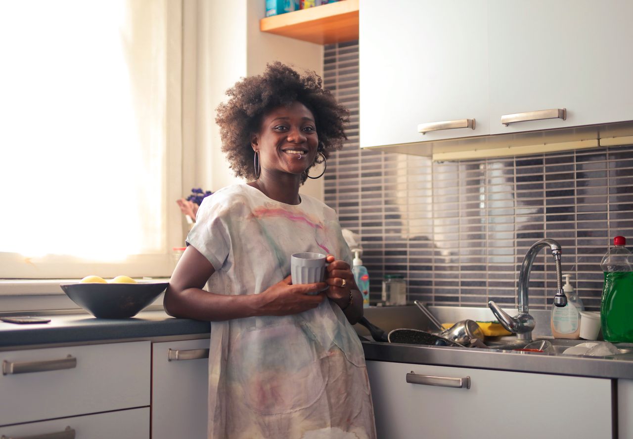 services-img A cheerful woman holding a cup in a bright kitchen, embodying a relaxed lifestyle.