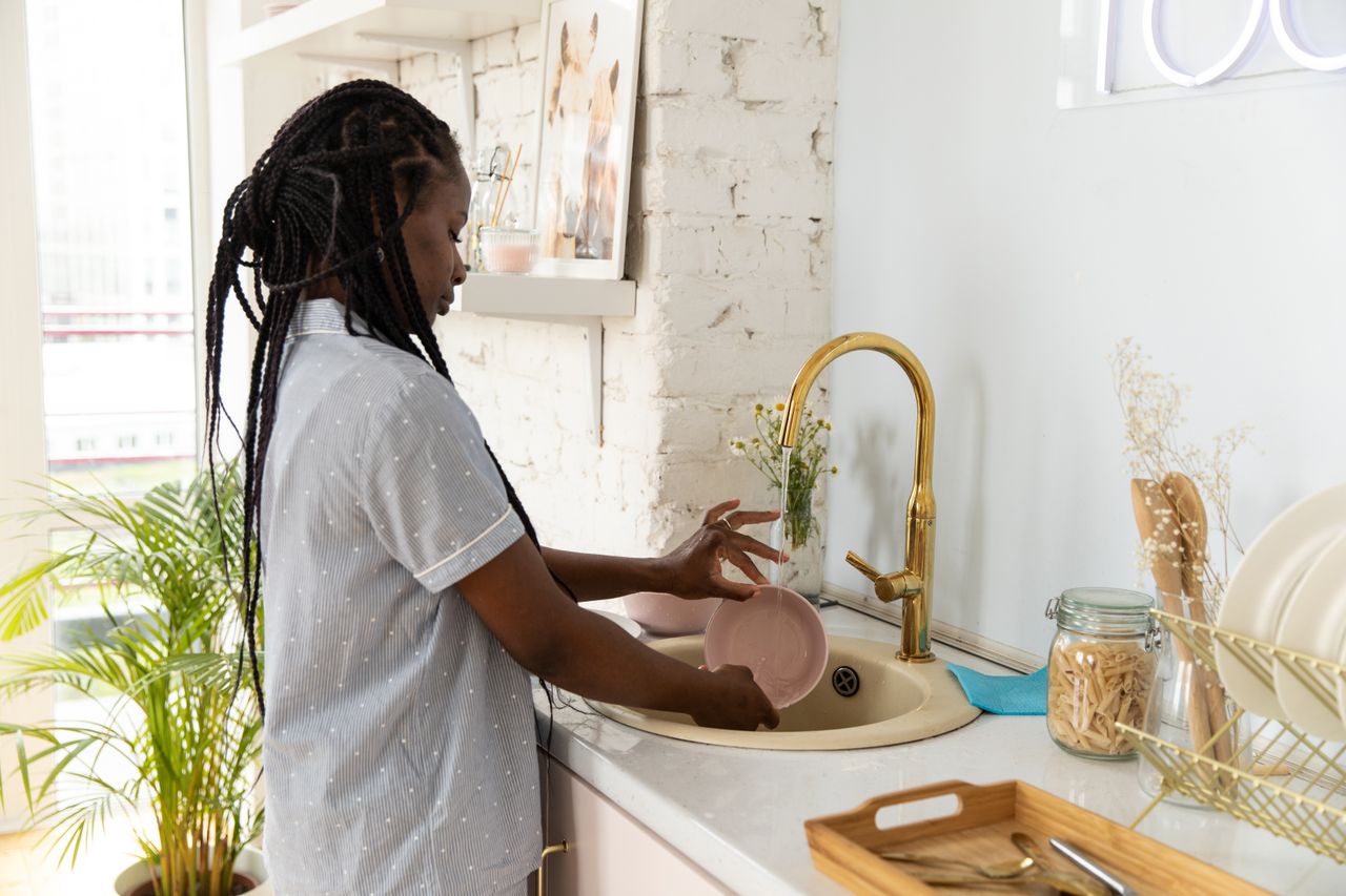 services-01 An adult woman washing dishes in a bright, modern kitchen setting.