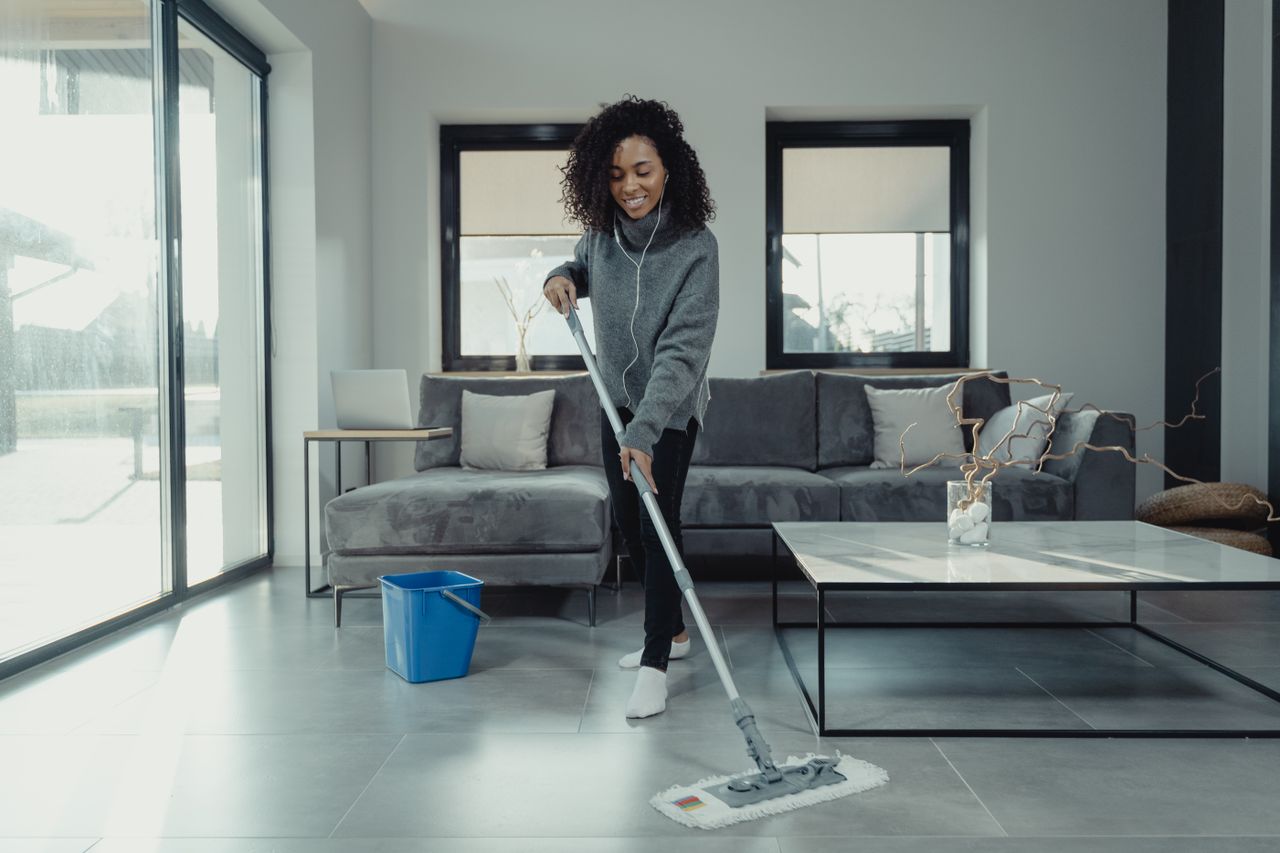 services-02 Woman mopping living room floor while listening to music in a cozy home setting.