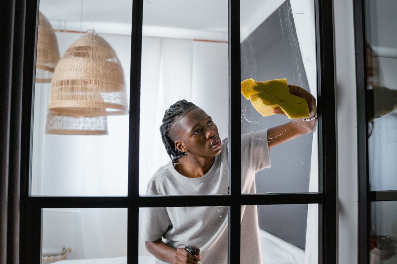 The Art of Drawing Readers In: Your attractive post title goes here A person attentively cleaning a glass window indoors with a yellow cloth, ensuring a spotless finish.